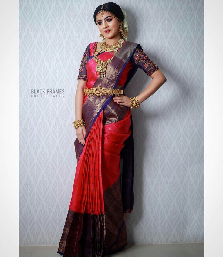 a woman in a red and brown sari with gold jewelry on her neck, standing against