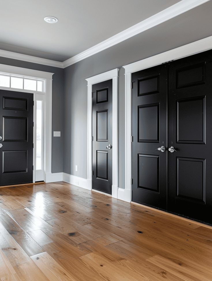 an empty room with three black doors and hard wood flooring on the hardwood floors