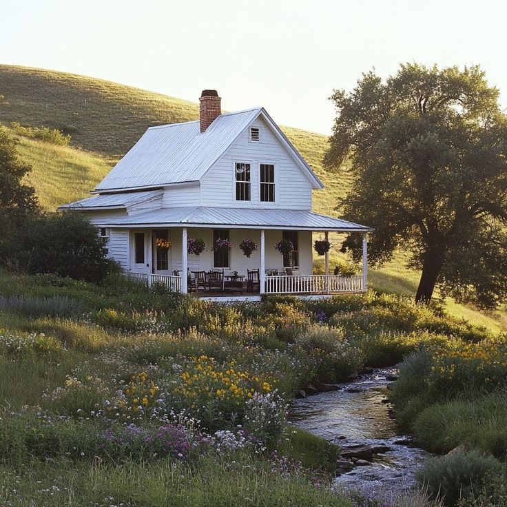 a white house sitting on top of a lush green hillside next to a river in front of it