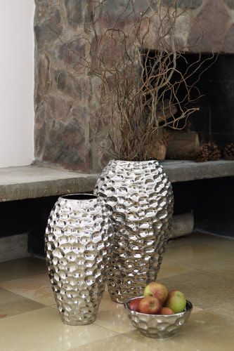 two silver vases sitting next to each other in front of a stone fire place