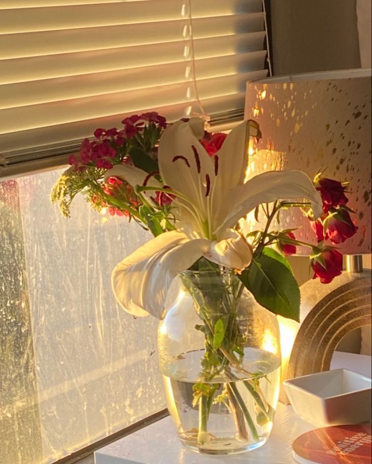 a vase filled with water and flowers on top of a table next to a window