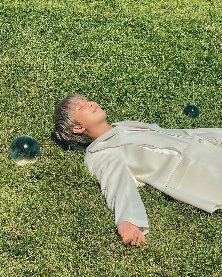 a man laying on the grass with balls in his hand and eyes closed, looking up