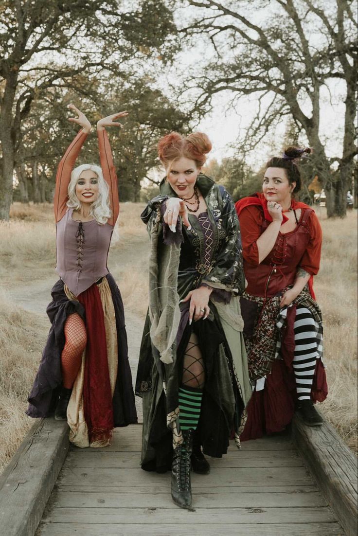 three women dressed in costume posing for the camera on a wooden platform with trees in the background