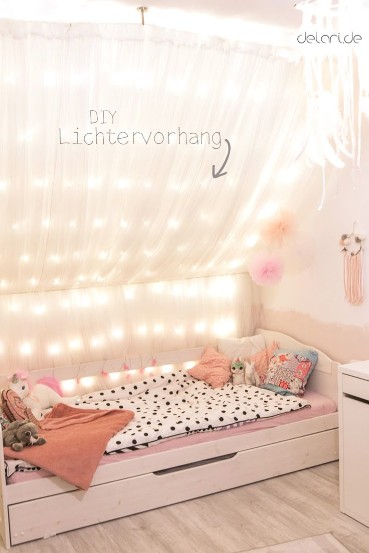 a white bed sitting under a window next to a light filled wall with lights on it