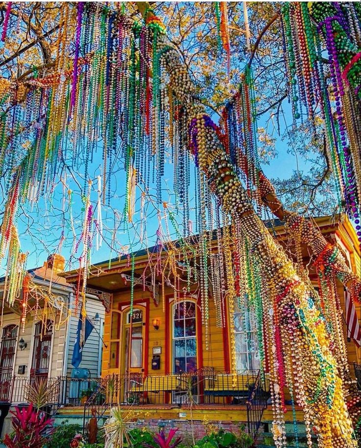 a tree with beads hanging from it's branches in front of a yellow house