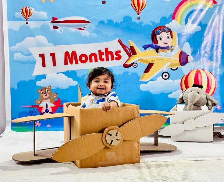 a baby sitting in a cardboard box with an airplane on it and other toys behind him