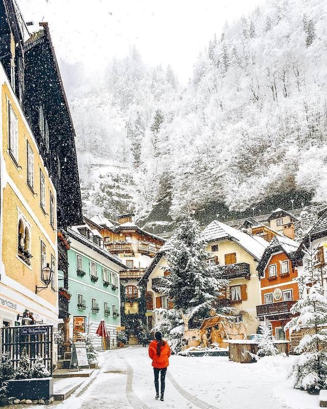 a woman walking down a snow covered street next to tall buildings in the middle of winter