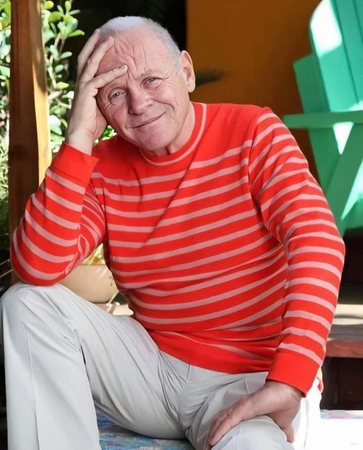 an older man sitting on a bench with his hand to his face and looking at the camera