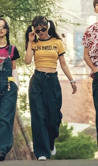 three girls walking down the street with one talking on her cell phone while wearing overalls