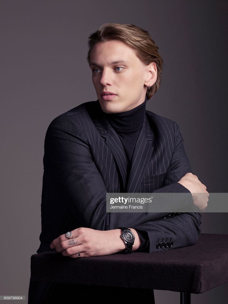 a man with his arms crossed sitting on a chair in front of a gray background