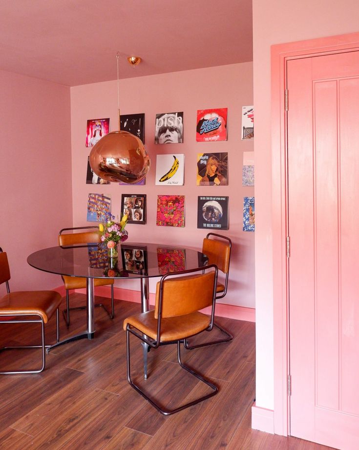 a dining room with pink walls and wooden flooring is pictured in this image, there are several chairs around the table