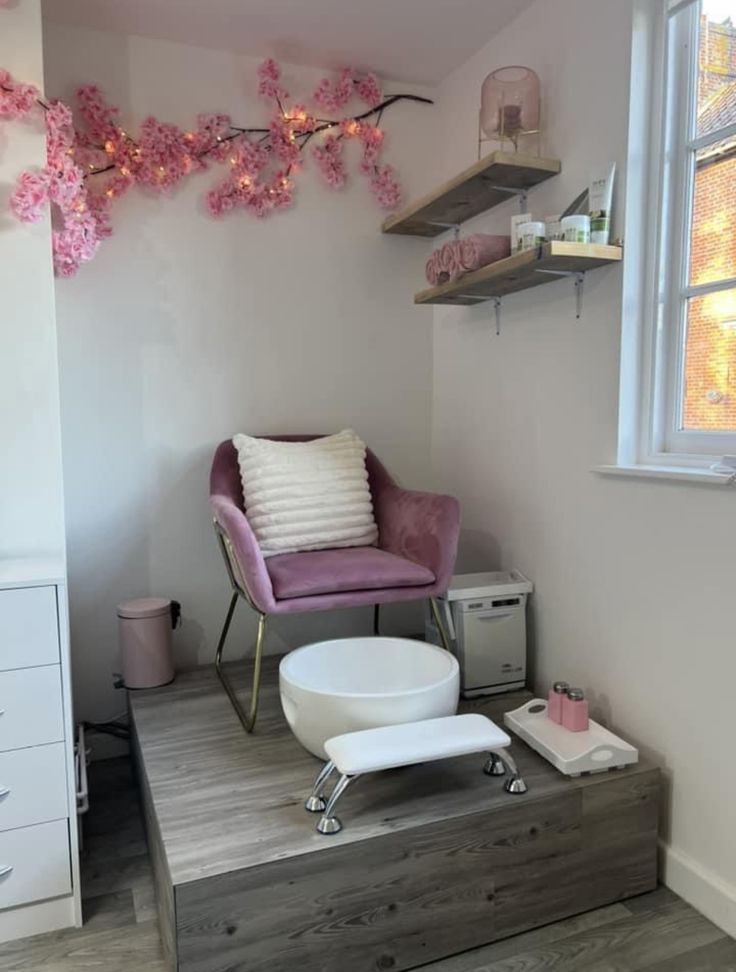 a pink chair sitting on top of a wooden platform next to a white dresser and window