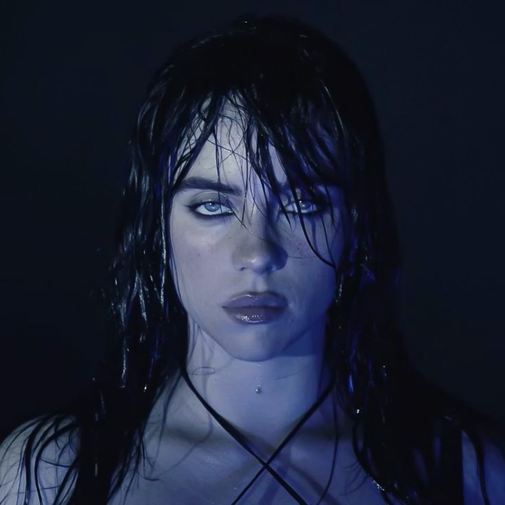 a woman with wet hair and blue eyes posing for a photo in the dark,