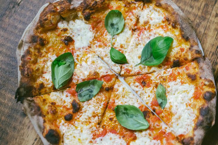 a pizza with cheese and spinach leaves on it sitting on a wooden table top