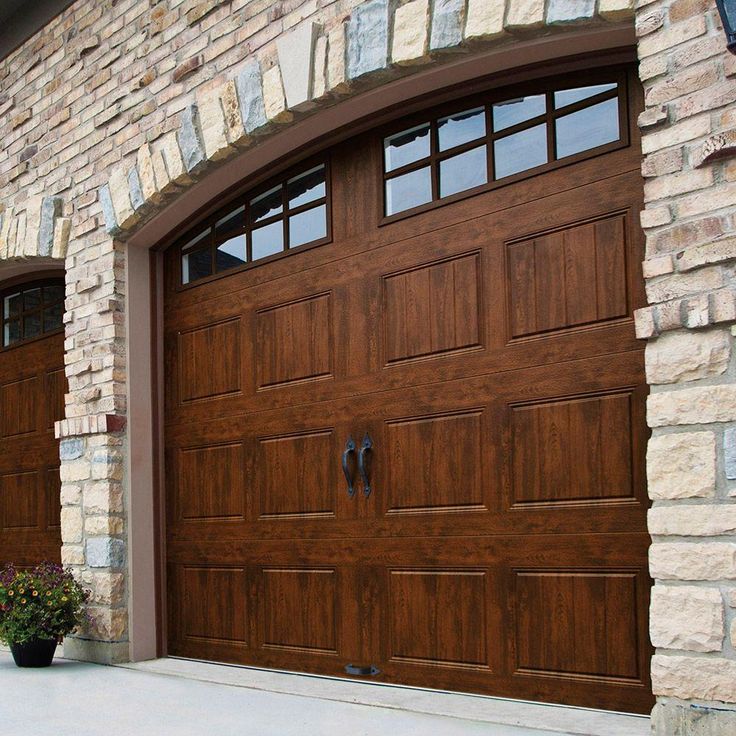 two brown garage doors in front of a brick wall and planter on the sidewalk