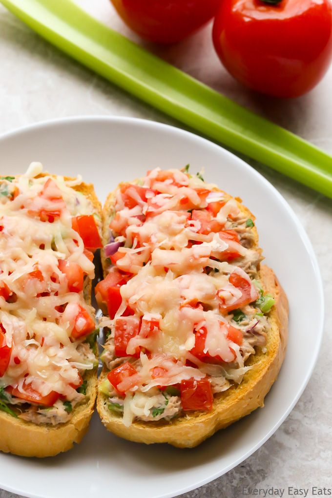 two pieces of bread on a plate with tomatoes and celery in the background