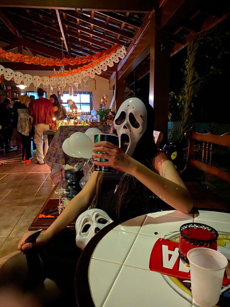 a woman sitting at a table with a mask on her face while taking a selfie