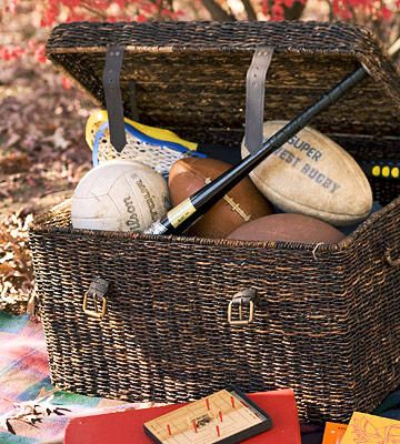 a wicker basket filled with different types of sports balls and equipment on a blanket