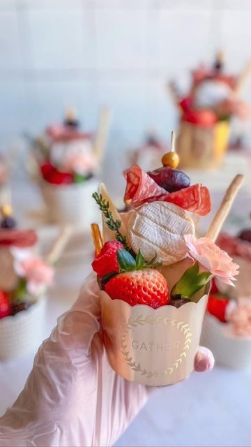 a hand holding up a cup filled with fruit and marshmallows on sticks