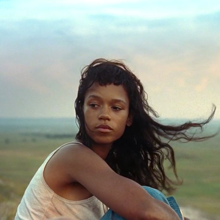 a young woman sitting on top of a wooden bench next to a lush green field