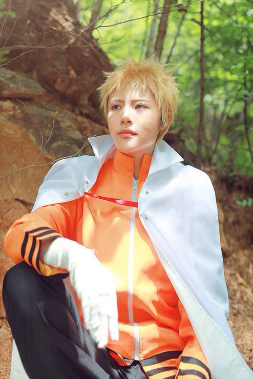 a person sitting on the ground wearing an orange and white outfit with black stripes, in front of some trees