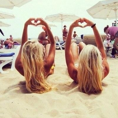 two women sitting in the sand making heart shapes with their hands while holding umbrellas