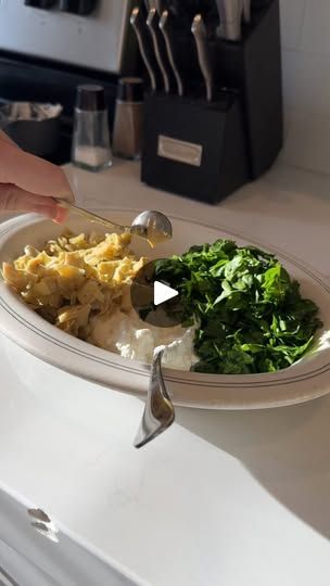 a person holding a spoon over a plate of food on a counter top next to a knife and fork