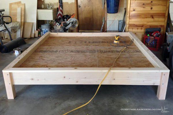 an unfinished bed frame in a garage with tools on the floor and other items around