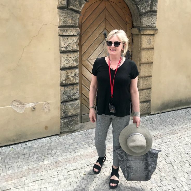 a woman standing in front of a building with a hat on her head and sunglasses on