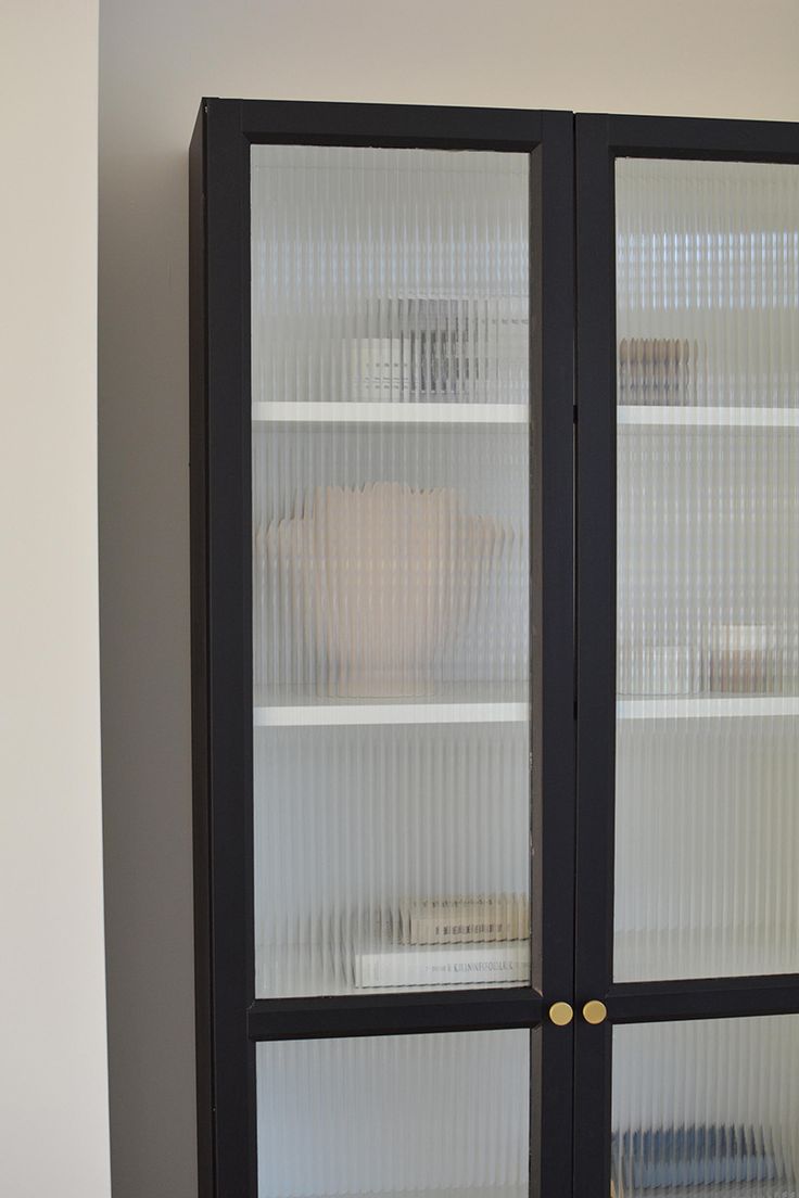 a black cabinet with glass doors in the corner next to a white vase and other items