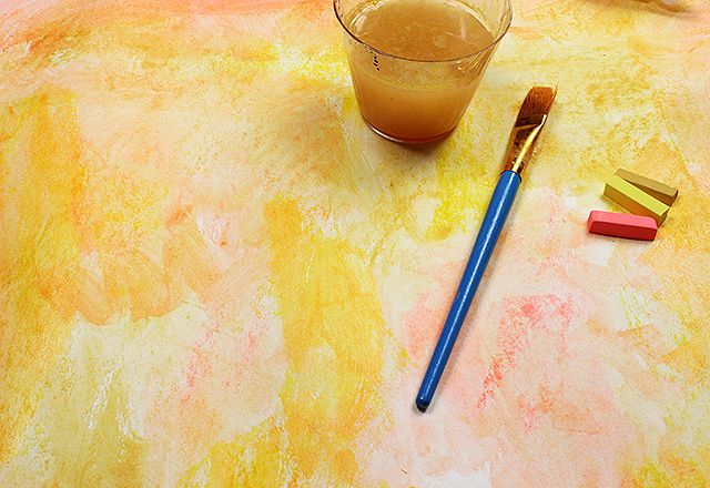 an orange liquid in a glass next to a blue and yellow brush on a table