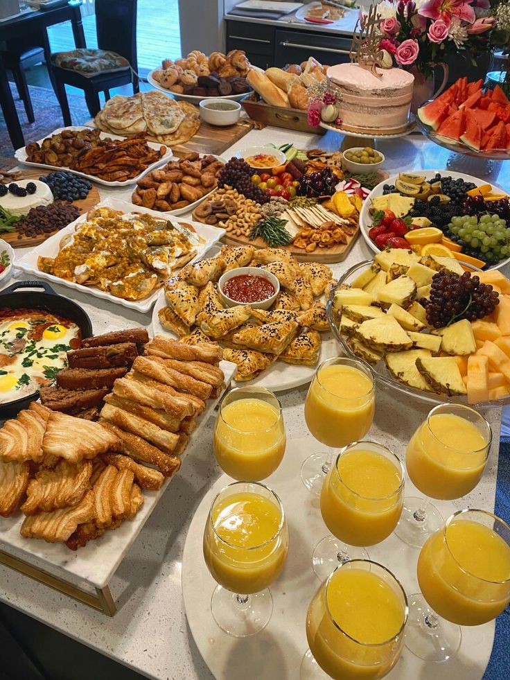 a table filled with lots of different types of food and glasses of orange juice in front of them