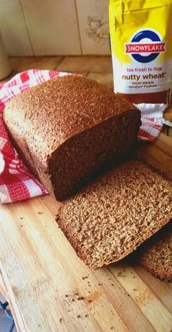 two loaves of bread sitting on top of a cutting board next to a bag of nutty wheat