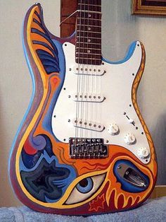 an electric guitar painted with colorful designs on it's body, sitting in front of a mirror