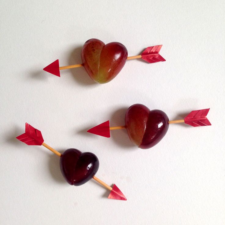 three heart shaped lollipops with arrows sticking out of them on a white surface