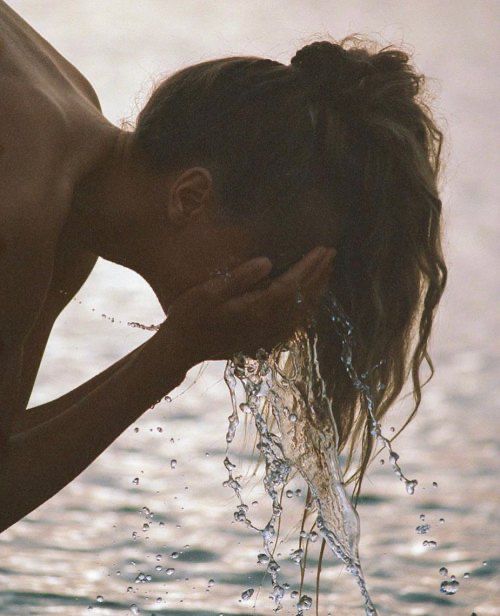 a woman standing in the water with her hand on her face as if she were kissing someone