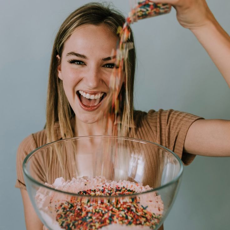 a woman is pouring sprinkles into a glass bowl with cereal in it