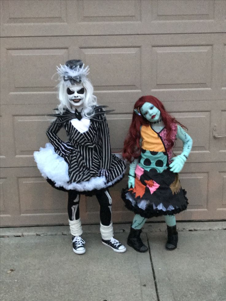 two children dressed up in costumes standing next to each other on the sidewalk near a garage door