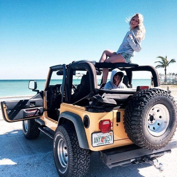 a woman sitting on the back of a yellow jeep next to a man in shorts