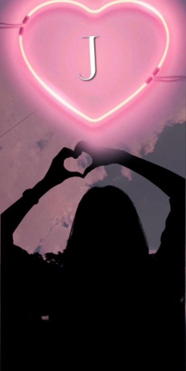 a woman holding her hand up in front of a neon heart with the letter j on it