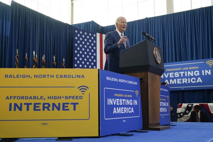 a man standing at a podium in front of an american flag and blue curtained wall