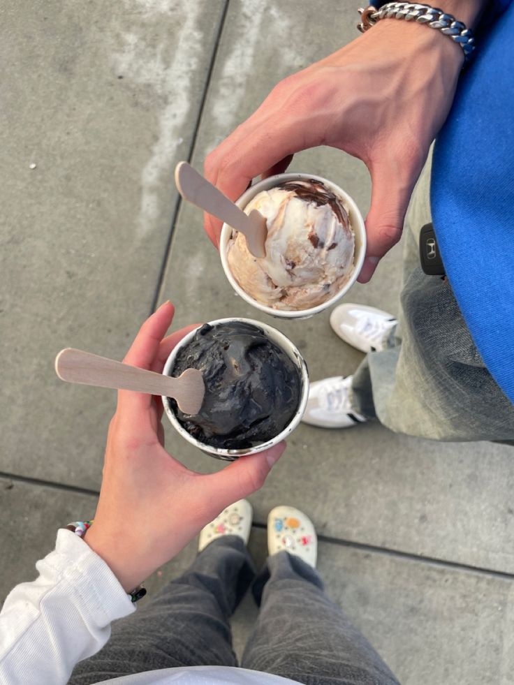 two people holding ice cream and spoons in their hands