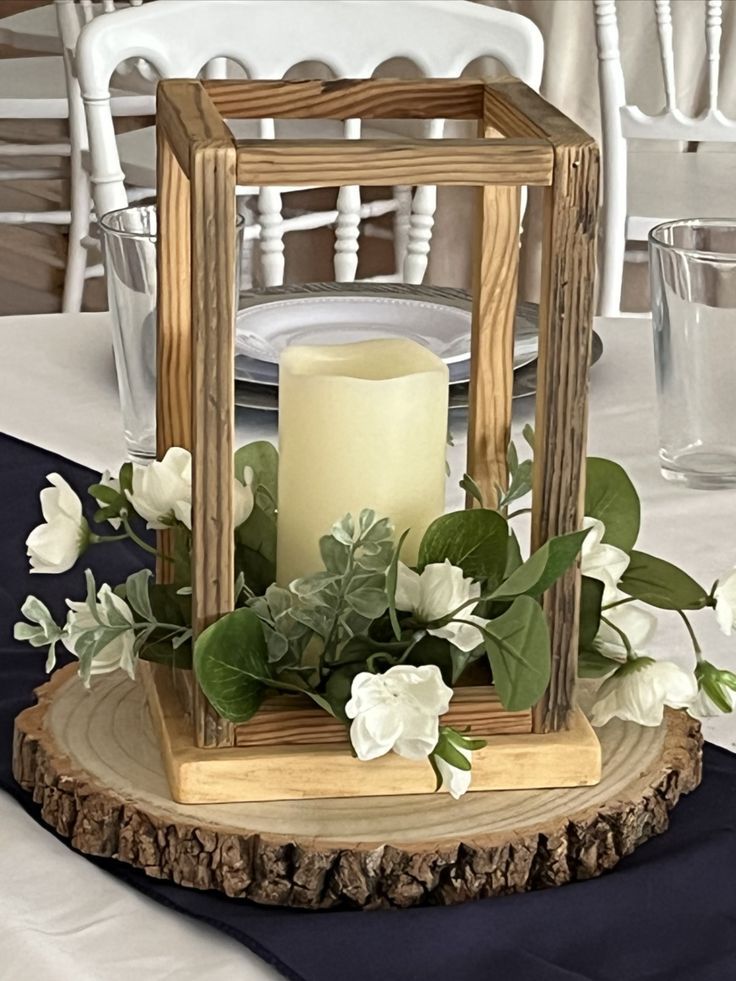 a candle is lit on top of a wooden stand with greenery and white flowers