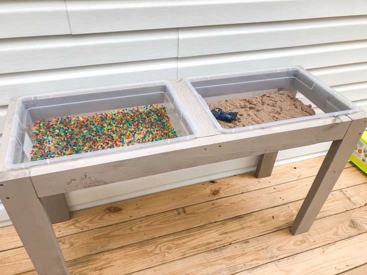 two plastic bins filled with sand and sprinkles on a wooden table