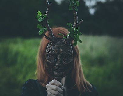 a woman with deer horns and antlers on her head is holding a stick in front of her face