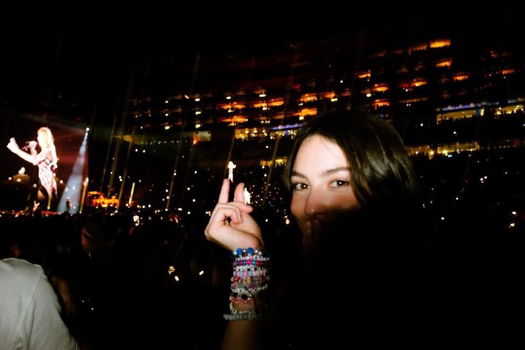 a woman making the peace sign in front of a large screen with a concert on it