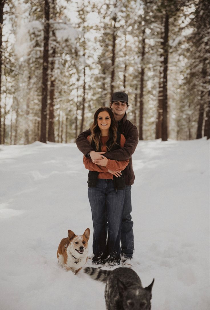 a man and woman are standing in the snow with two dogs, one is brown and white