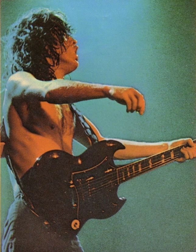 a man with no shirt on playing an electric guitar and holding his right arm out