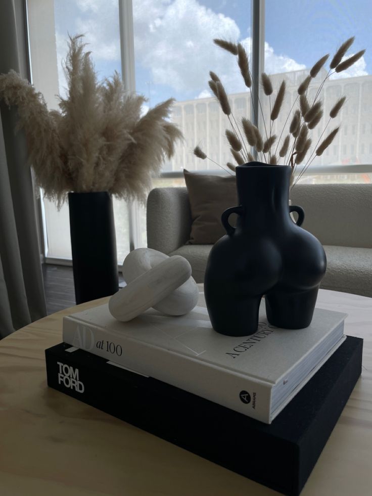 two black vases sitting on top of a book next to a plant and window