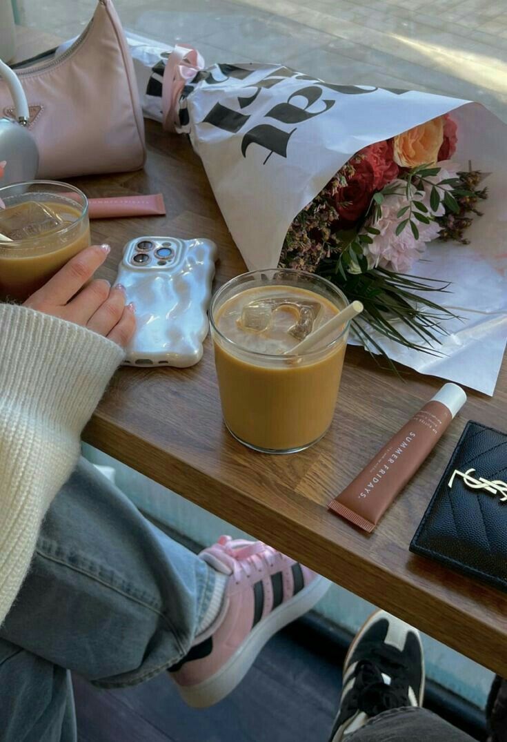 a person sitting at a table with some food and drinks on it, next to a cell phone